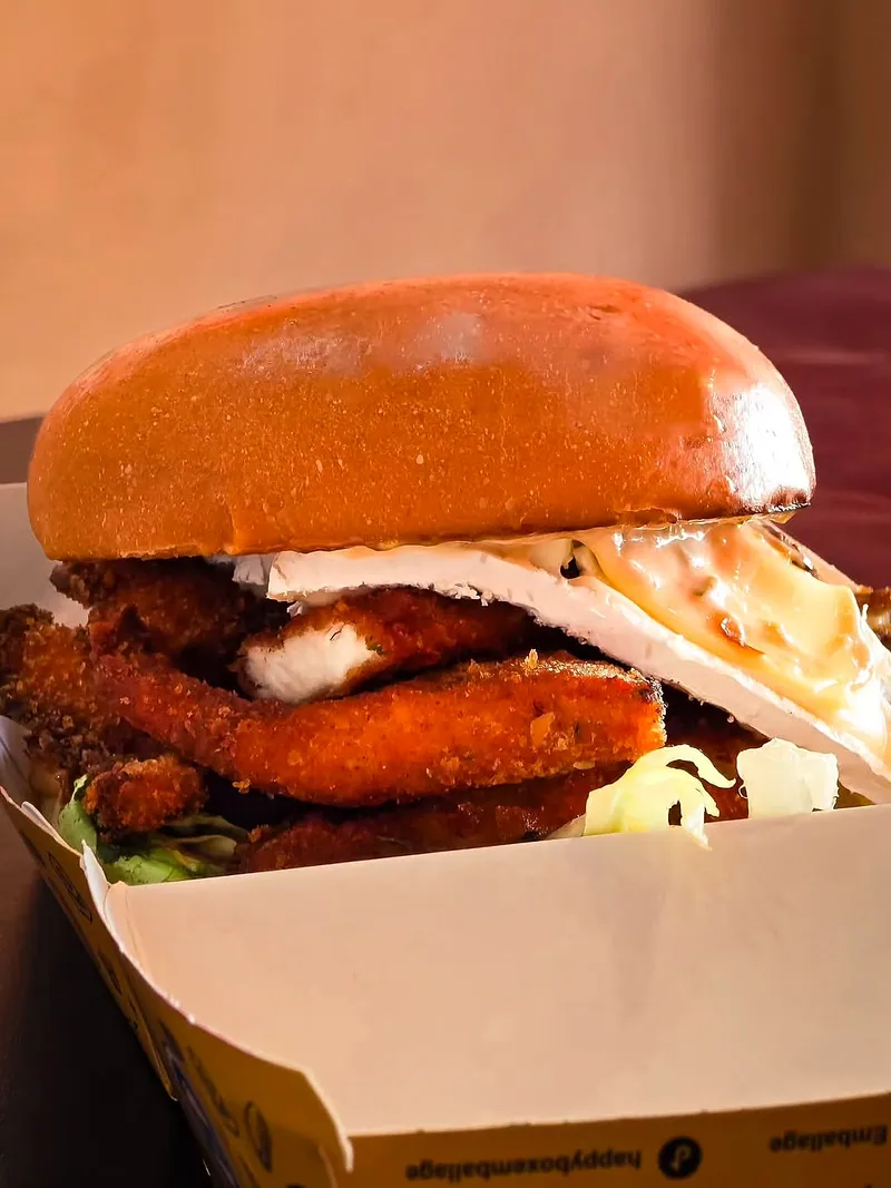 Un burger au poulet pané, sauce blanche et salade dans une boîte ouverte