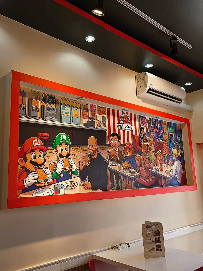 La fresque murale de la salle : des personnages de dessin animé attablés devant des burgers, sous le logo Whoopy Burger