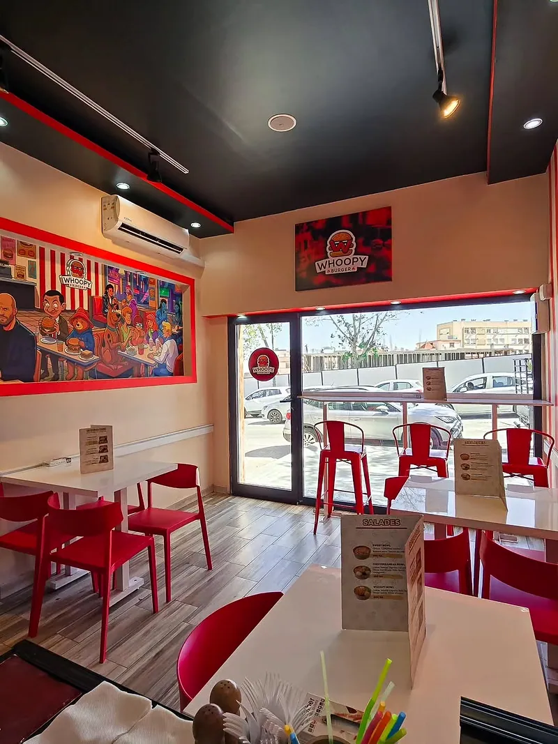 L’intérieur de Whoopy Burger : salle lumineuse aux rayures rouges et blanches, tables blanches et chaises rouges